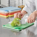A person in a white coat cutting a piece of broccoli on a blue and white San Jamar Saf-T-Grip cutting board.