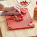 A person cutting meat on a San Jamar red cutting board.