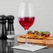 A Stolzle Bordeaux wine glass filled with red wine sits on a table next to a cutting board with crackers and strawberries.