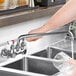 A hand holding a Waterloo wall-mounted faucet over a sink.