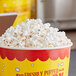 A bucket of Pop Weaver white butterfly popcorn kernels on a table with a label that says freshly popped.