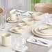 A table set with Acopa Pangea fog white porcelain bowls and white dishes and silverware.