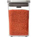 An OXO Good Grips clear square plastic food storage container with a stainless steel lid containing red granules.