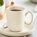 An Acopa Pangea fog white porcelain cup on a saucer with coffee