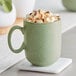 A sage green Acopa Pangea porcelain mug filled with hot chocolate and marshmallows.