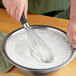 An OXO Good Grips whisk stirring white powder in a bowl.
