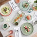 A table with Acopa Pangea fog white matte porcelain pasta bowls, plates, and utensils on it.