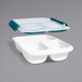 An OXO white rectangular food storage container with a three sectioned tray inside.