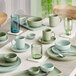 A table set with white plates and sage green cups from Acopa Pangea.