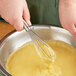 A person using an OXO SteeL narrow piano whisk to mix yellow batter in a bowl.