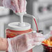 A gloved hand using a Choice condiment pump to pour sauce into a container.