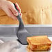 A hand holding a black OXO Good Grips nylon spatula over a toasted sandwich.