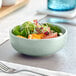 A bowl of salad with tomatoes, greens, and fruit in a blue Acopa Pangea nappie bowl.