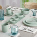 A table set with a blue Acopa Pangea nappie bowl and clear glass on a table with plates and cups.