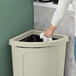 A hand holding a white bag puts a tissue in a Lavex beige corner round trash can with a lid.