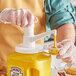 A hand using a Choice condiment pump to pour mustard into a plastic container.