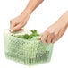 A person holding a green OXO plastic basket with lettuce inside.