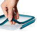 A hand holding an OXO Prep & Go rectangular plastic container with a blue lid.