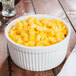 A white fluted souffle bowl filled with macaroni and cheese on a wooden table.