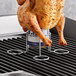 A chicken on a stainless steel can on a grill.