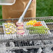 A person using a Mr. Bar-B-Q stainless steel perforated grill sheet to cook vegetables on a grill.