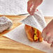 A person wearing a plastic glove wraps a sandwich in Choice Cafe Deli Sandwich Wrap Paper.