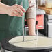 A person using a Carnival King aluminum crepe batter spreader to make a crepe on a pan.