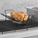 A whole chicken cooking on a Fox Run non-stick carbon steel roasting rack over a grill.