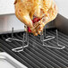 An Outset stainless steel beer can chicken roaster with prongs on a grill.