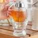 A person using a Fox Run glass honey dispenser to pour honey into a glass jar.