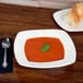 A CAC porcelain square soup plate with soup and bread on a table.