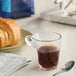 A glass of Lavazza Dek decaf espresso on a table with a croissant.