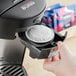 A hand putting a Lavazza Gran Riserva coffee pod in a black coffee machine.