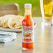 A bottle of Marie Sharp's Hot Habanero Hot Sauce on a table with a plate of burritos.