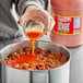 A person pouring Marie Sharp's Beware Comatose Habanero Hot Sauce into a pot.