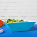 A blue rectangular GET Keywest melamine bowl filled with a salad on a table.