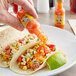 A hand holding a small bottle of Marie Sharp's Garlic Habanero hot sauce over tacos.