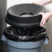 A hand opening a black round funnel lid on a black trash can.