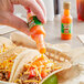 A hand pouring Marie Sharp's Mild Habanero hot sauce onto a taco.