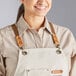 A woman wearing an Acopa Hazleton cream canvas bib apron with leather straps.