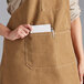 A woman wearing a brown Acopa Hazleton canvas bib apron with 3 pockets.