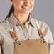 A woman wearing a brown Acopa Hazleton canvas bib apron with cross-back straps and three pockets.