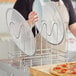 A woman in a kitchen uses a GI Metal pizza screen rack to hold a pizza.