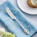 An Acopa Ophelia stainless steel butter knife on a blue napkin next to a plate of bread.