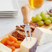 A cheese platter with a cheese fork on a wooden board with dried apricots and fruit.