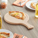 A cheese pizza on a Choice wooden serving board with a slice on a plate.