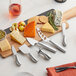 A cutting board with various cheeses and Acopa cheese knives on a table.