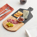 An Acopa acacia wood and slate serving board with cheese, grapes and crackers on it.