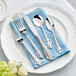 A white plate with Acopa Ophelia stainless steel flatware on a blue towel.