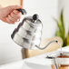 A person using an Acopa stainless steel gooseneck kettle to pour water over coffee.